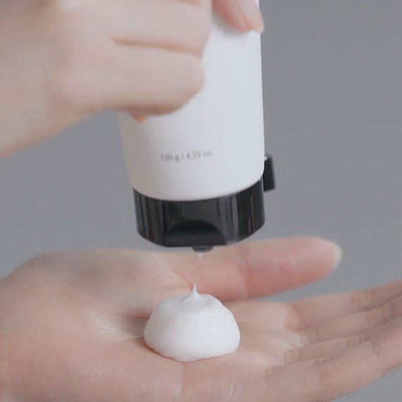 A hand holding the Snow Enzyme Cleanser EX tube dispensing white foam texture onto the palm