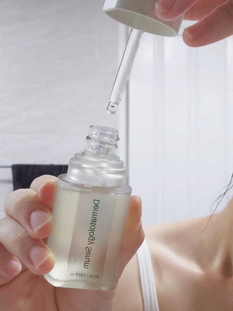 Self-loading dropper lifted from the Dermatology Serum bottle, a clear drop forming at the tip