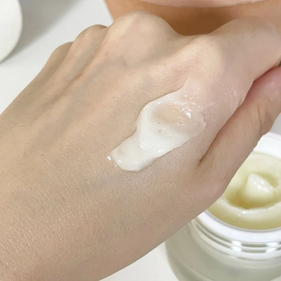 Glossy swatch of Dermatology Cream on the back of a hand, open jar in the corner