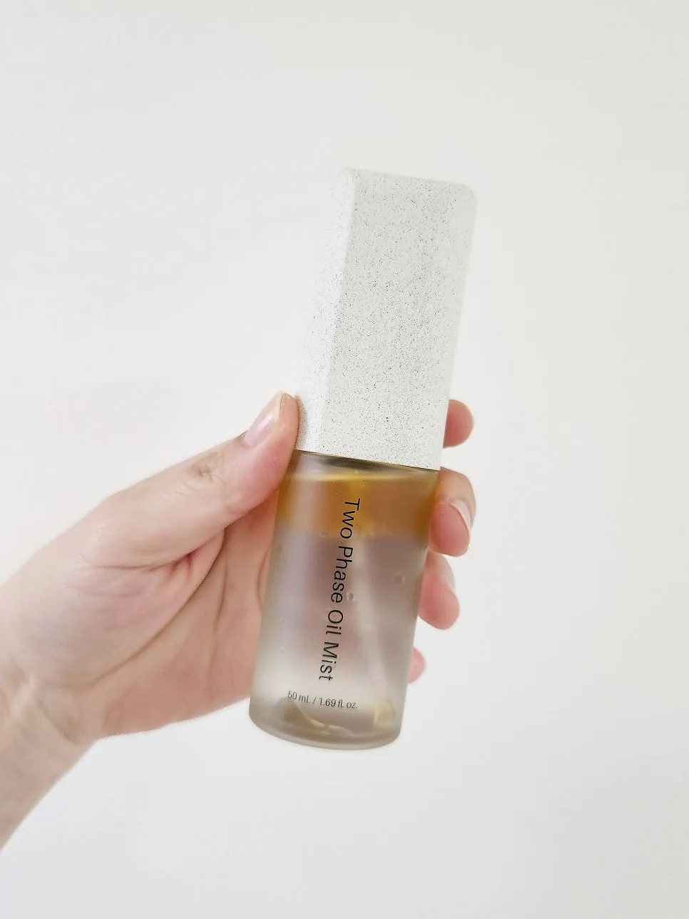 Hand holding the Two Phase Oil Mist with a golden oil layer floating on top of the clear watery layer