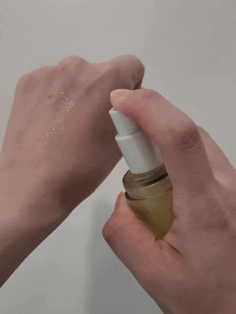 Fingers pressing the spray pump of the oil mist over the back of a hand at close range