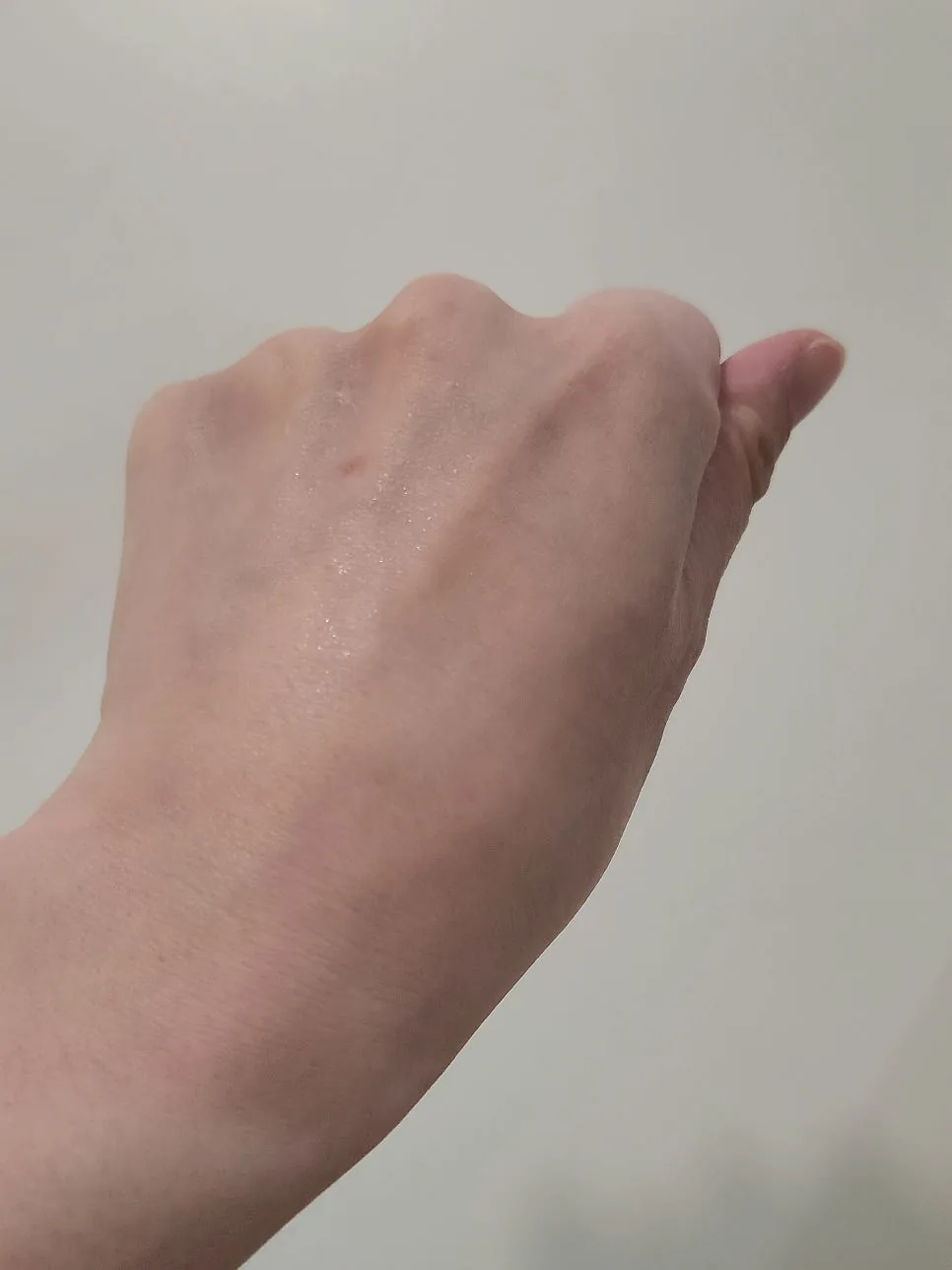 Back of a hand after one spray, showing a fine dewy sheen rather than an oily film